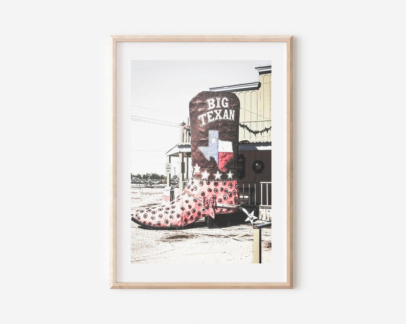 May include: A large, pink and white cowboy boot with a brown top and the words "Big Texan" on it. The boot is in front of a building with a Texas flag on it.