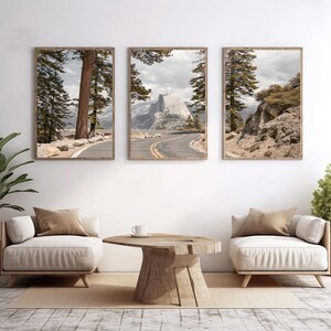 May include: Three framed landscape prints featuring scenic views of a mountain road and towering trees. The prints are displayed above two cream-colored armchairs and a wooden coffee table, creating a serene living room setting.