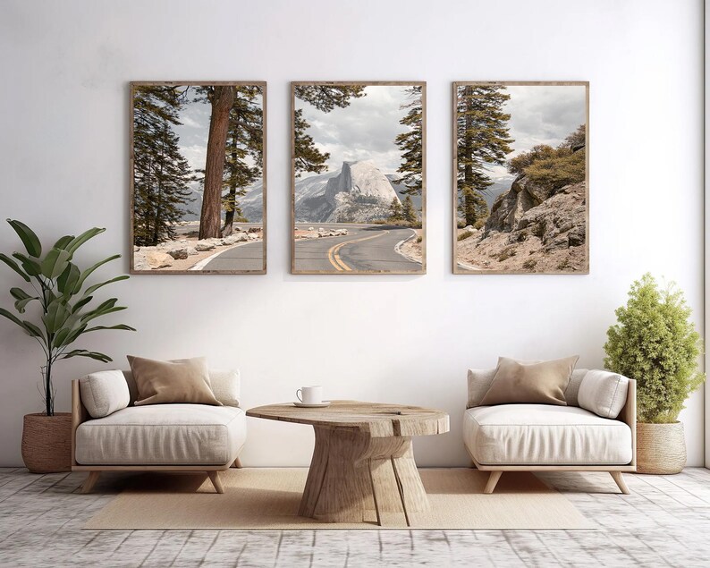 May include: Three framed landscape prints featuring scenic views of a mountain road and towering trees. The prints are displayed above two cream-colored armchairs and a wooden coffee table, creating a serene living room setting.