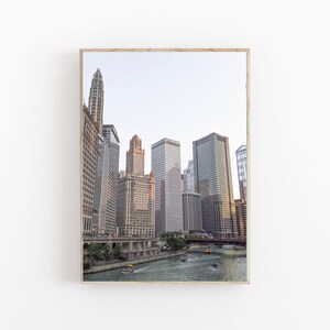 May include: A photograph of a cityscape with tall buildings and a river in the foreground. The buildings are mostly gray and brown, and the river is a light blue. There are boats on the river.