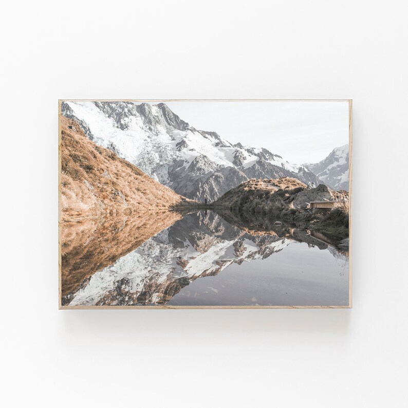Puede incluir: Una fotograf&iacute;a panor&aacute;mica de un lago de monta&ntilde;a que refleja los picos nevados de las monta&ntilde;as circundantes. El agua est&aacute; tranquila y clara, reflejando perfectamente el cielo y las monta&ntilde;as. Las monta&ntilde;as est&aacute;n cubiertas de nieve y hielo, y el cielo es de un azul suave.