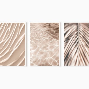 May include: A set of three abstract prints featuring close-up textures of sand, water, and a palm leaf. The prints are in shades of beige and brown.