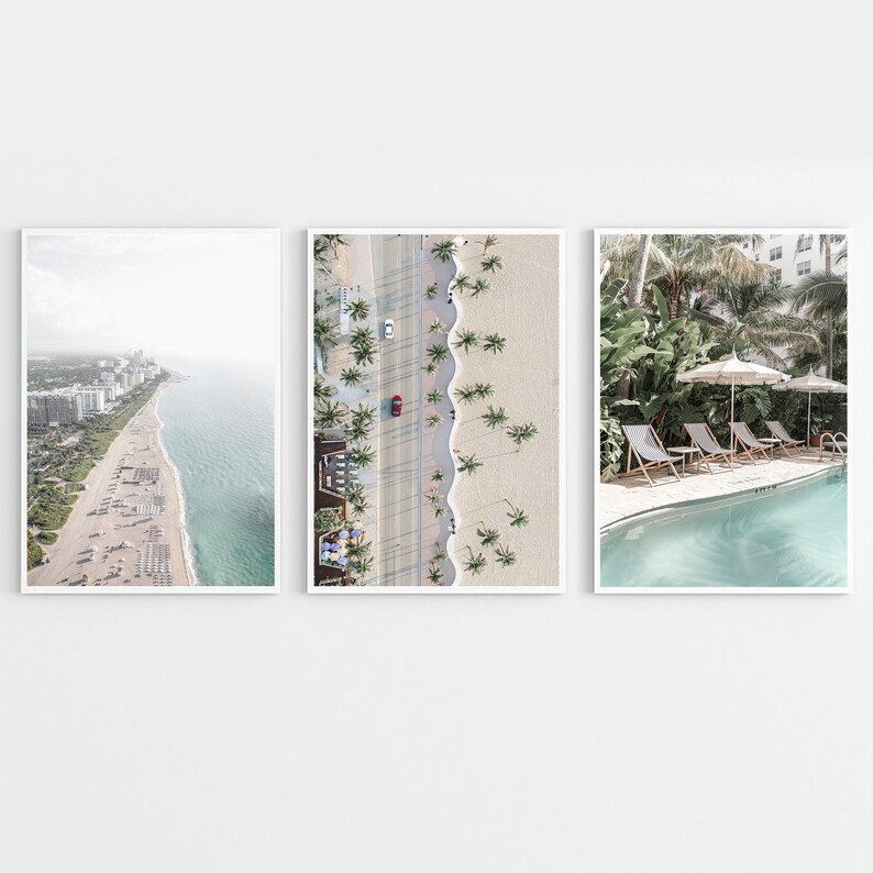 May include: Three framed prints of beach scenes. The first print shows an aerial view of a beach with white sand, blue water, and palm trees. The second print shows a close-up of a beach with palm trees and a red car driving down the road. The third print shows a pool with lounge chairs and palm trees.