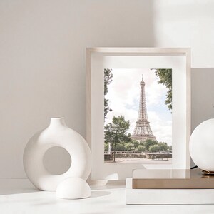 May include: A white framed picture of the Eiffel Tower in Paris, France. The picture is on a white shelf with a white vase and a white sphere.