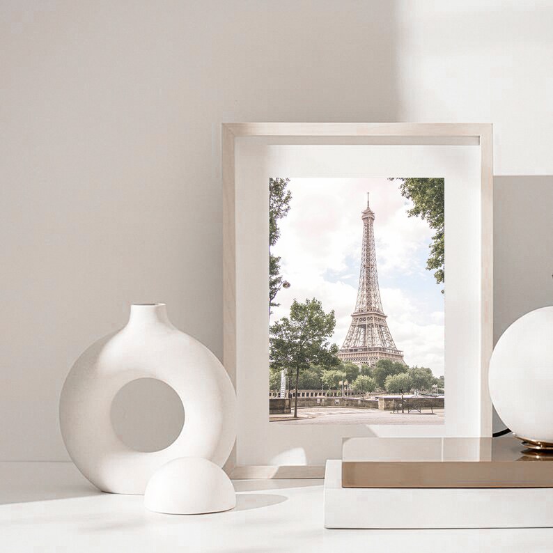 May include: A white framed picture of the Eiffel Tower in Paris, France. The picture is on a white shelf with a white vase and a white sphere.