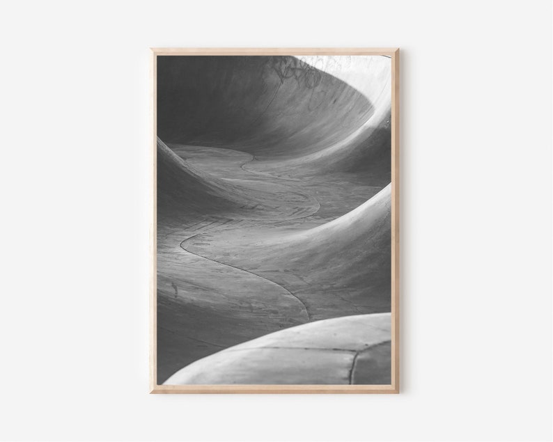 May include: Black and white photograph of a concrete skate park ramp. The ramp is curved and has a smooth, textured surface.