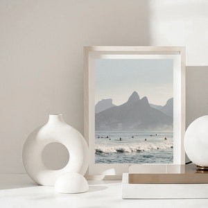 May include: A white ceramic vase with a large circular opening in the center, a white ceramic sphere, and a framed photograph of a beach scene with mountains in the background.
