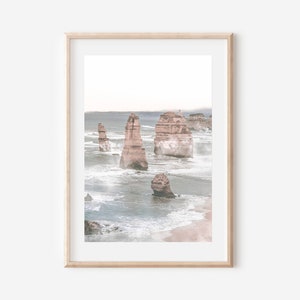 May include: A framed photograph of a seascape with tall rock formations rising from the ocean. The water is a light blue and white, with waves crashing against the rocks. The sky is a pale blue, and there is a hint of fog in the distance.