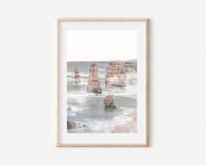 May include: A framed photograph of a seascape with tall rock formations rising from the ocean. The water is a light blue and white, with waves crashing against the rocks. The sky is a pale blue, and there is a hint of fog in the distance.
