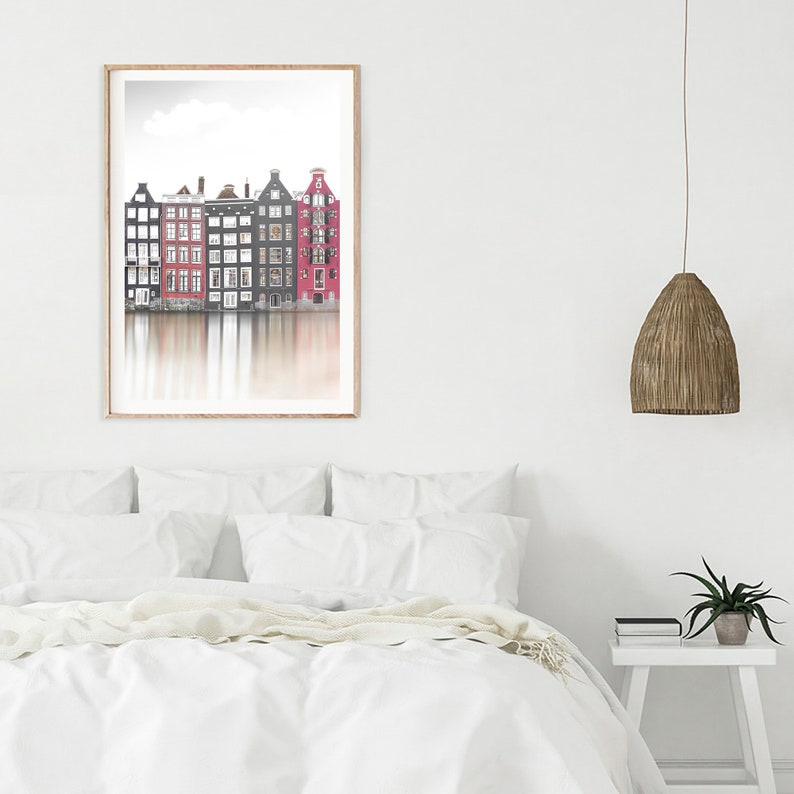 May include: A framed photograph of a row of colorful houses reflected in a canal. The houses are a mix of red, black, and white. The sky is a light blue with a few clouds.