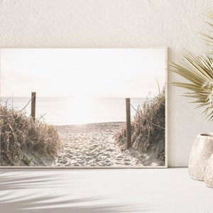 May include: A framed photograph of a sandy beach path leading to the ocean. The path is lined with tall grasses and the ocean is a hazy blue in the distance.