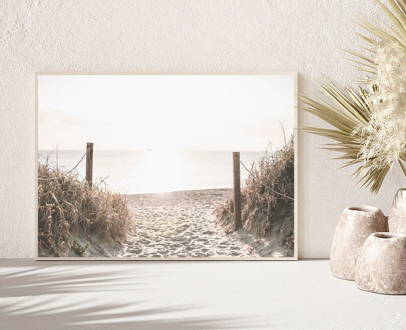 May include: A framed photograph of a sandy beach path leading to the ocean. The path is lined with tall grasses and the ocean is a hazy blue in the distance.