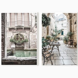 May include: Two framed art prints. The left print shows a Venetian canal scene with a gondola. The right print depicts a stone courtyard with tables, chairs, and lush greenery. The prints have a muted color palette.