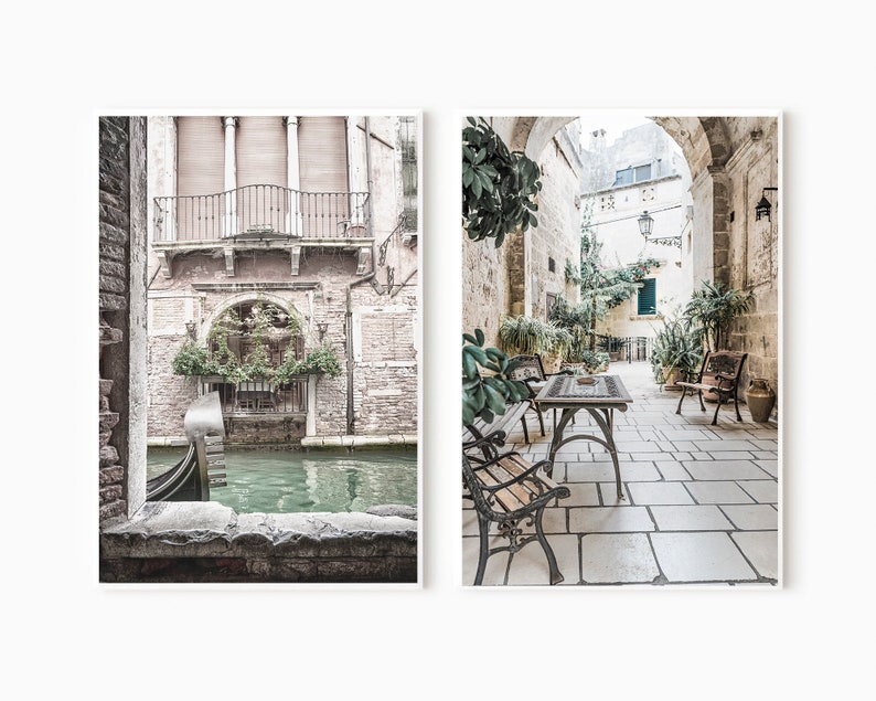 May include: Two framed art prints. The left print shows a Venetian canal scene with a gondola. The right print depicts a stone courtyard with tables, chairs, and lush greenery. The prints have a muted color palette.