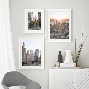 May include: Three framed photographs of cityscapes. The top left photo shows a street in a city with tall buildings. The top right photo shows a cityscape with a sunrise in the background. The bottom photo shows a cityscape with a river in the foreground.