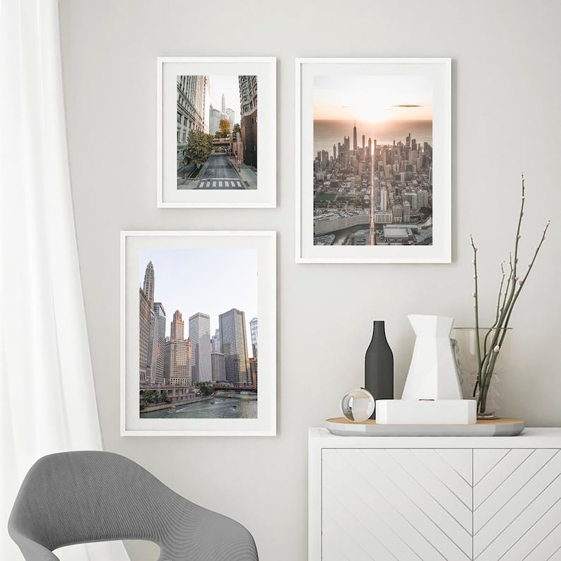 May include: Three framed photographs of cityscapes. The top left photo shows a street in a city with tall buildings. The top right photo shows a cityscape with a sunrise in the background. The bottom photo shows a cityscape with a river in the foreground.