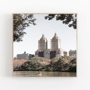 May include: A photograph of a city skyline with two tall buildings in the center. The buildings are surrounded by trees and a lake. The sky is a light blue color.