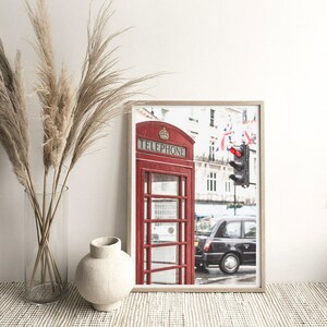 May include: A red telephone booth with the word "TELEPHONE" on the front, located on a street in London, England. The booth is in front of a black taxi cab and a traffic light.