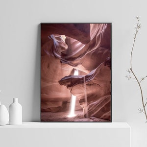 May include: A photograph of a narrow canyon with a beam of light shining through the opening. The canyon walls are a deep red color and the light creates a dramatic contrast.