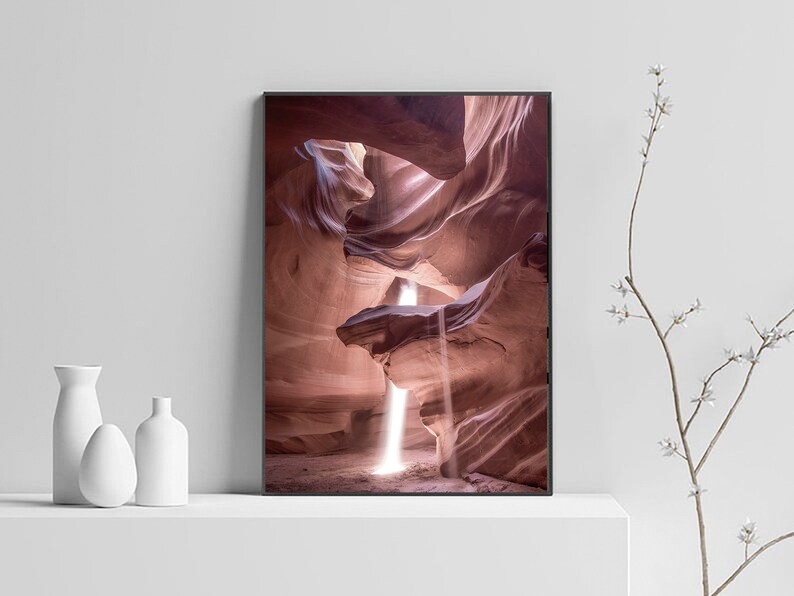 May include: A photograph of a narrow canyon with a beam of light shining through the opening. The canyon walls are a deep red color and the light creates a dramatic contrast.