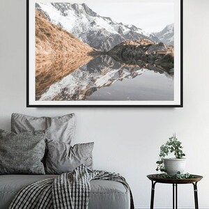 Puede incluir: Una fotograf&iacute;a enmarcada de un lago de monta&ntilde;a con monta&ntilde;as cubiertas de nieve que se reflejan en el agua. Las monta&ntilde;as son de color marr&oacute;n claro y el agua es de color azul claro.