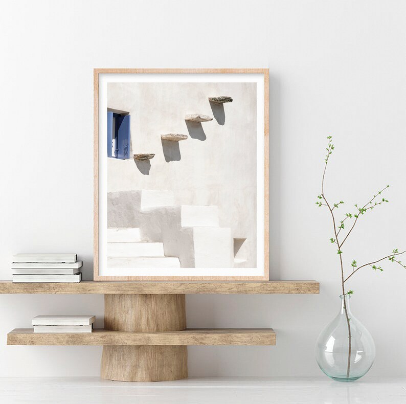 May include: A framed photograph of a white building with a blue door and a set of stone steps leading up to it. The steps are cast in shadow, creating a geometric pattern on the wall.