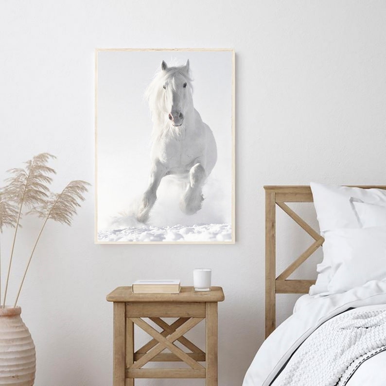 May include: A white horse runs through a snowy field, its mane and tail flowing in the wind. The horse is in focus, while the background is blurred.