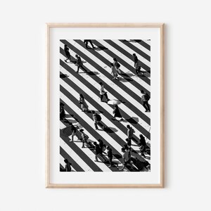 May include: Black and white photo of people walking across a crosswalk with diagonal stripes. The photo is taken from above, and the people's shadows are visible on the ground.