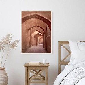 May include: A photograph of a long, narrow hallway with arched ceilings. The walls are a warm, reddish-brown color, and the floor is a light brown. The hallway is lit by natural light coming in from the end of the hallway.