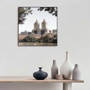 May include: A framed photograph of a city skyline with two tall buildings in the center. The buildings are surrounded by trees and a body of water. The photo is in a black frame and is hanging on a white wall.