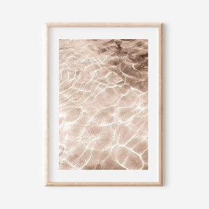 May include: Abstract photograph of rippling water in shades of brown and white. The water is calm and still, with a soft, ethereal glow.