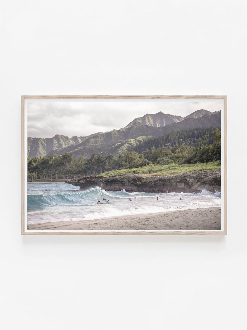 May include: A scenic photograph of a beach with turquoise water and white sand.  The beach is framed by lush green mountains and a rocky cliff.  People are swimming and surfing in the water.