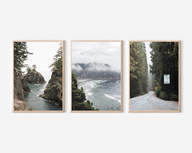 May include: Set of three framed landscape prints. The prints feature coastal and forest scenes with muted tones. One print shows a rocky coastline, another a misty beach, and the third a road through a forest with a sign that reads "Welcome to Oregon."