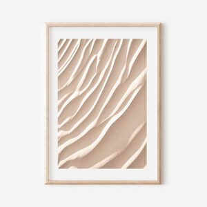 May include: A framed print of a close-up of sand dunes with a light beige color and a textured, wavy pattern.