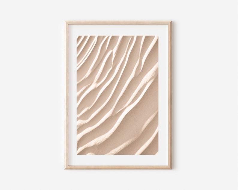 May include: A framed print of a close-up of sand dunes with a light beige color and a textured, wavy pattern.