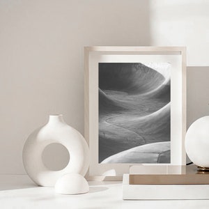 May include: A black and white photograph of a concrete skate park, framed in a white frame. The photo is displayed on a white surface with a white ceramic vase and a white ceramic sphere.