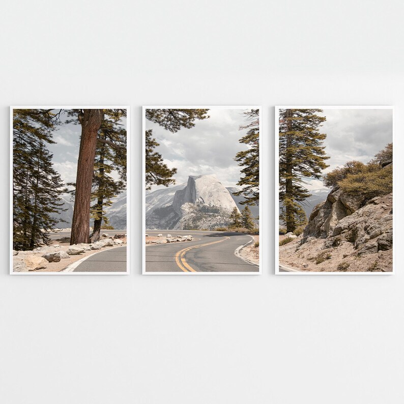May include: Set of three framed landscape prints featuring scenic views of a winding road through a mountainous region. The prints showcase a road with yellow lines, trees, and a mountain under a cloudy sky. The color palette includes shades of gray, brown, and green.