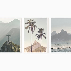 May include: A set of three minimalist landscape prints featuring a mountain range, palm trees, and a beach scene with surfers. The prints are in muted tones of blue and gray.