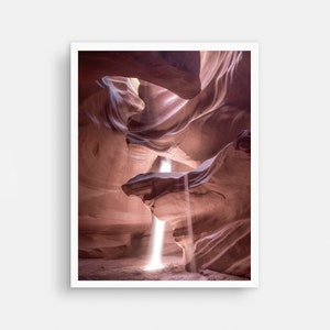 May include: A narrow canyon with smooth, red rock walls. A beam of light shines through a crack in the ceiling, illuminating the canyon floor.