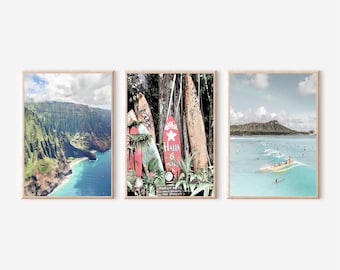 May include: Three framed prints depicting Hawaiian scenery. The first print shows a green, lush mountainside with a blue ocean and a sandy beach. The second print shows a close-up of a group of surfboards leaning against a tree trunk. The third print shows a view of a beach with surfers riding waves in the ocean.