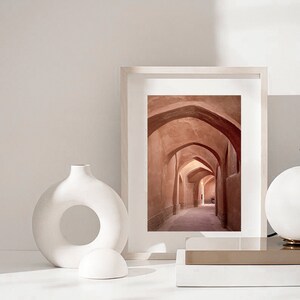May include: A framed photograph of a narrow, arched hallway with terracotta walls and a light brown floor. The hallway is lined with arches on both sides, creating a sense of depth and perspective.