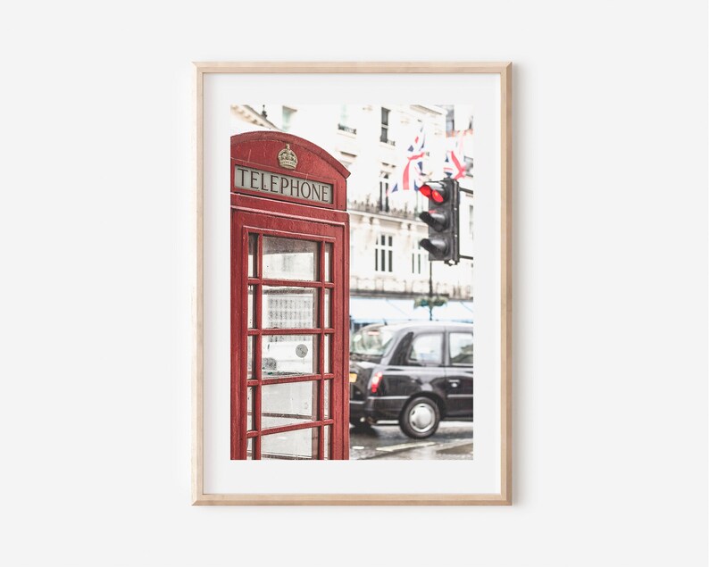 May include: A red telephone booth with the word "TELEPHONE" on the front, a black taxi cab, and a traffic light with a red light on in the background. The scene is set in London, England.