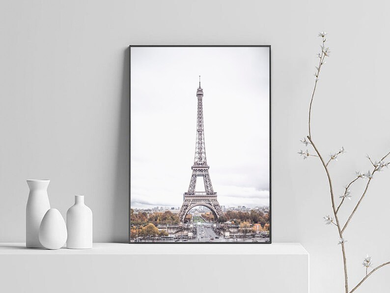 May include: A black and white photograph of the Eiffel Tower in Paris, France. The tower is in the center of the image and is surrounded by trees and buildings. The sky is cloudy and gray.