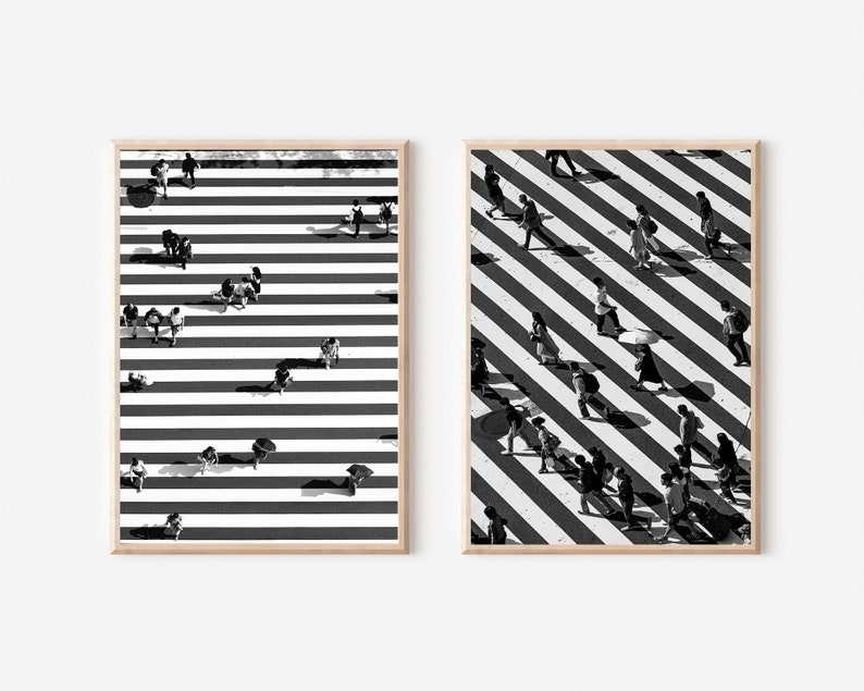 May include: Two black and white photographs of people walking across a crosswalk. The crosswalk is a black and white striped pattern. The people are all wearing different clothes and are walking in different directions. The photos are framed in a light wood frame.