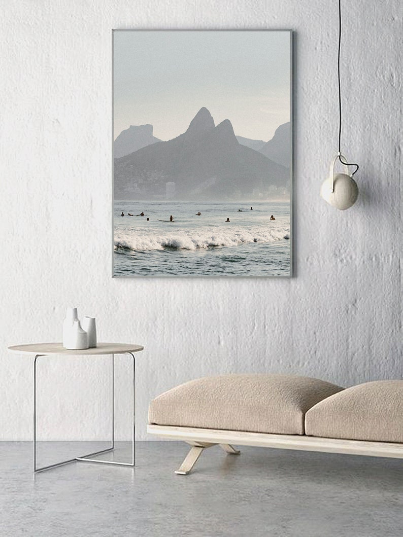 May include: A framed photograph of a beach scene with a mountain range in the background. The water is blue and there are waves crashing on the shore. There are people surfing in the water.