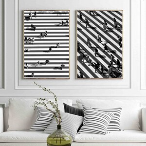 May include: Two black and white prints of a crosswalk with people walking across. The prints are framed and hanging on a white wall.