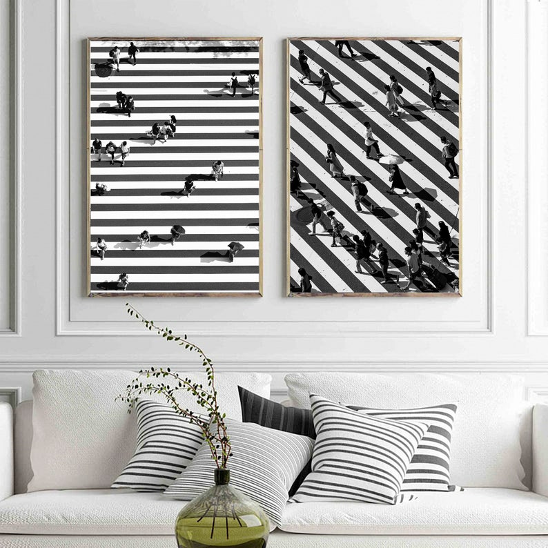 May include: Two black and white prints of a crosswalk with people walking across. The prints are framed and hanging on a white wall.