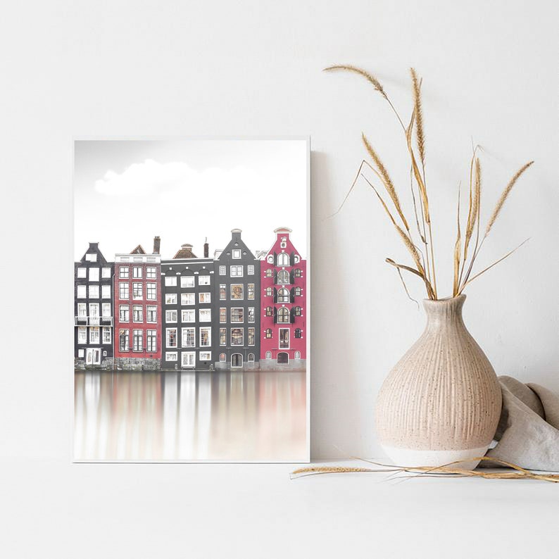 May include: A black and white photograph of a row of colorful buildings reflected in a canal. The buildings are a mix of red, black, and white, and they have many windows. The water is calm and still, and the sky is cloudy.
