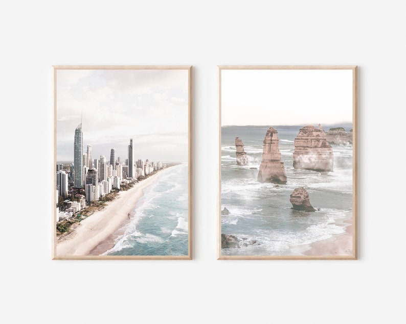 May include: Two framed prints of coastal scenes. The first print shows a city skyline with tall buildings along a sandy beach with blue ocean waves. The second print shows a rocky coastline with large rock formations in the ocean.