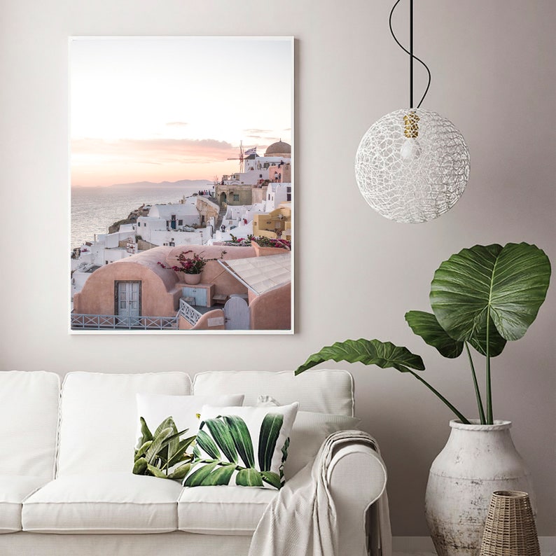 May include: A framed photograph of a white and pink village with a windmill on a cliff overlooking the ocean at sunset.